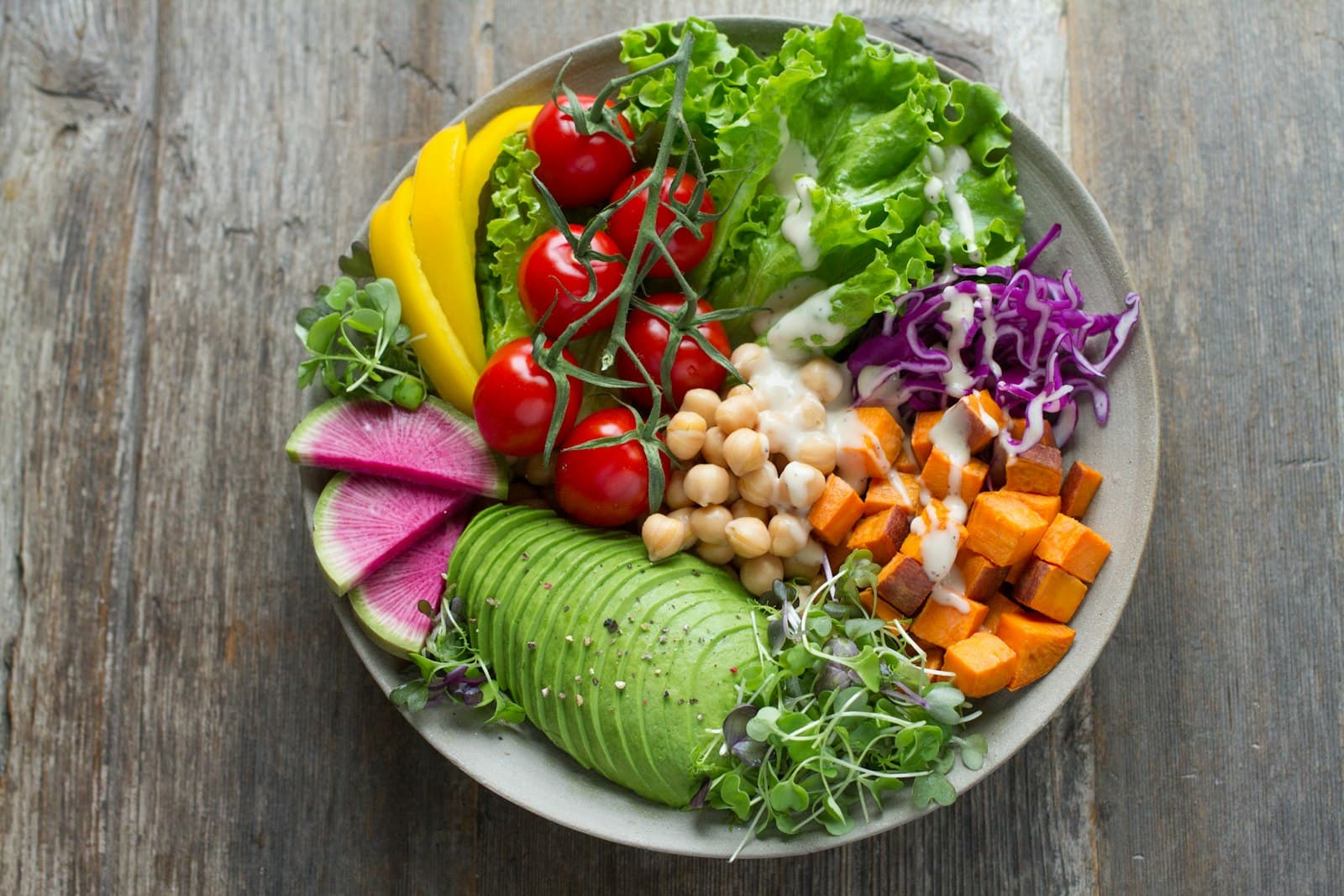 A colorful Buddha bowl with avocado, vegetables, and whole foods on a wooden surface